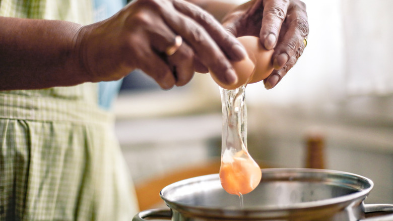 woman's hands cracking egg into saucepan