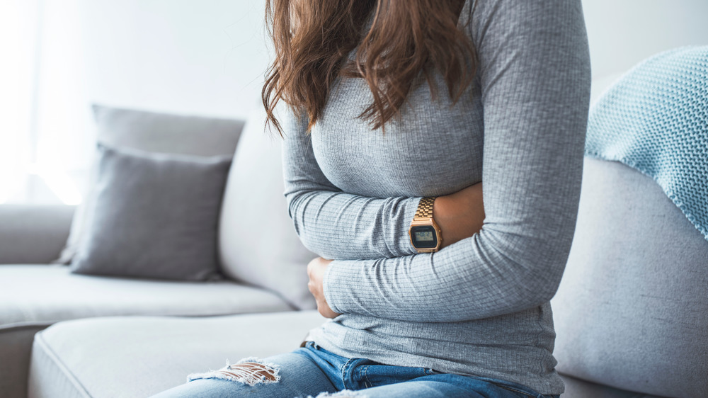 Woman sitting on couch holding stomach in pain
