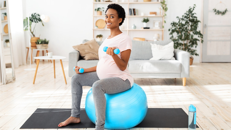 pregnant woman lifting weights while sitting on an exercise ball