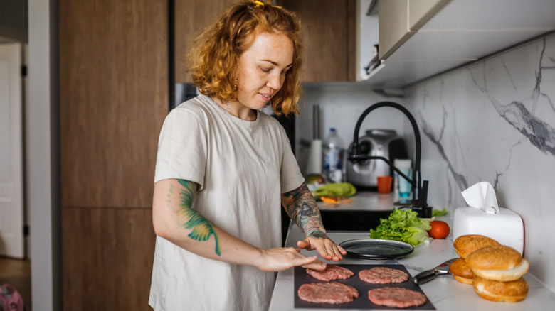 A woman patting out four hamburgers on a cutting board