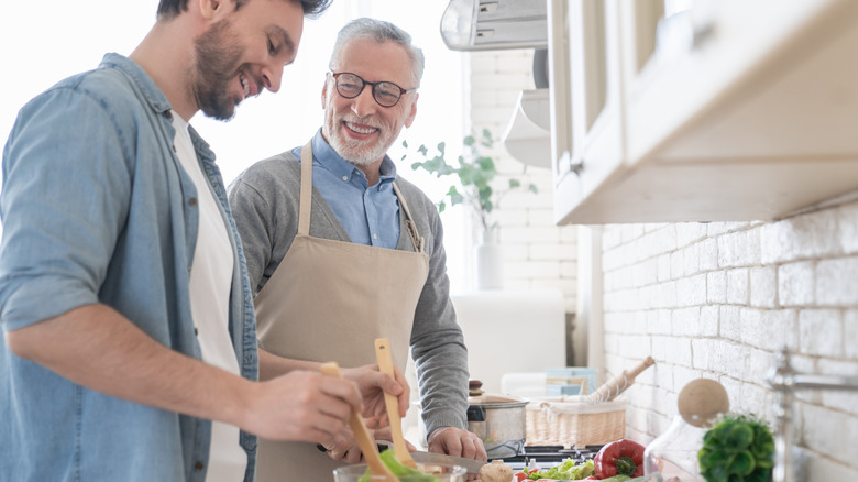 younger and older man preparing meal in kitchen
