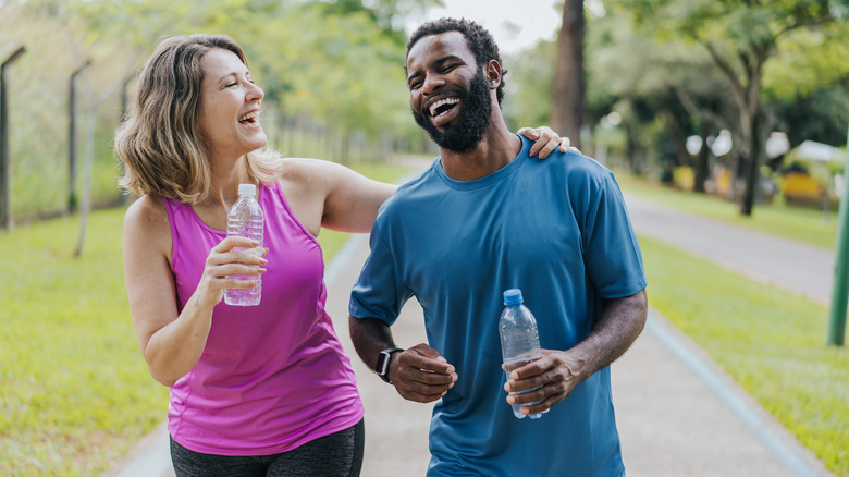man and a woman drinking bottled water while walking