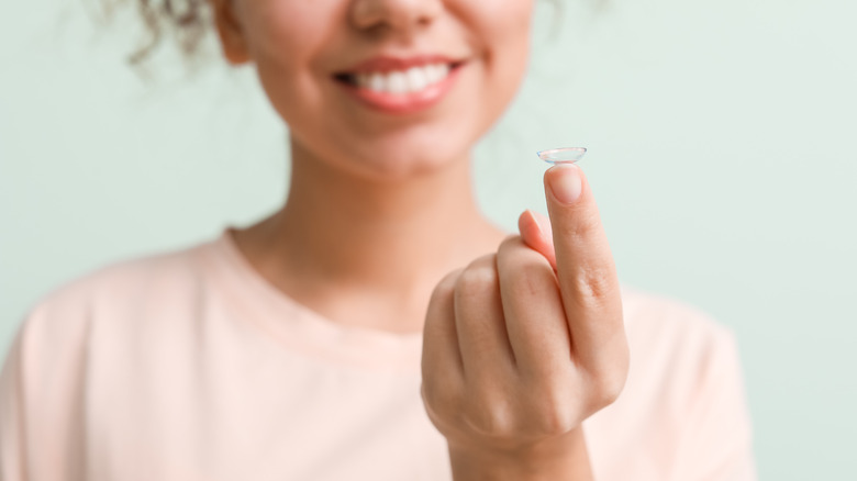 A woman holds a contact lens on her fingertips