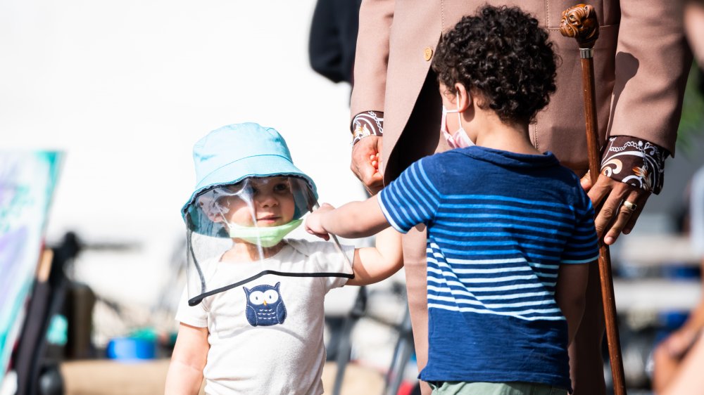 A child wearing a face shield and another wearing a mask compare looks