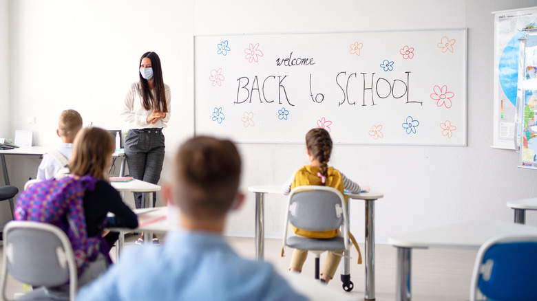 Teacher with face mask welcoming children back at school