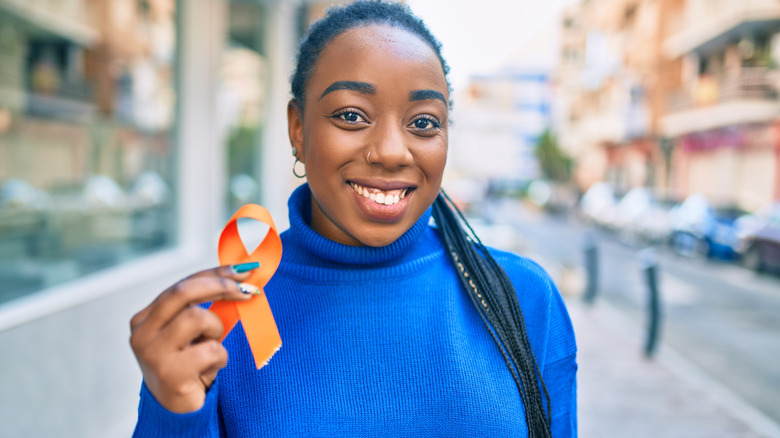 Smiling woman holds orange MS ribbon on city street