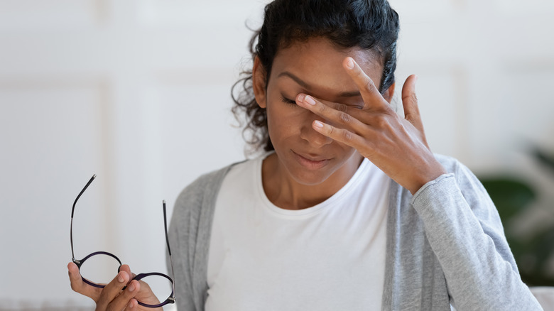 Woman removes her glasses and holds her hand to her forehead