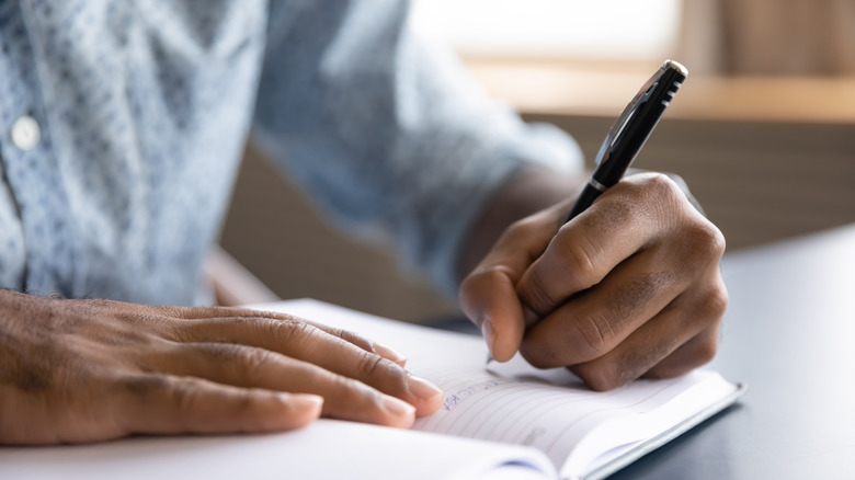 Left hand holding a pen and writing in journal