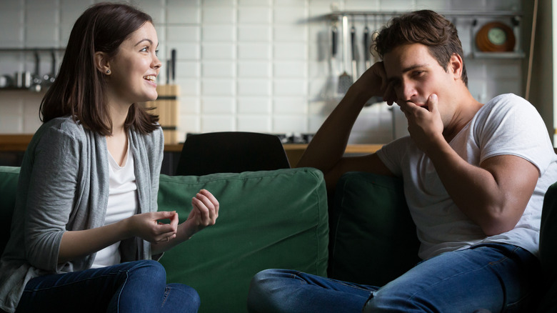 Man yawning while seated opposite woman