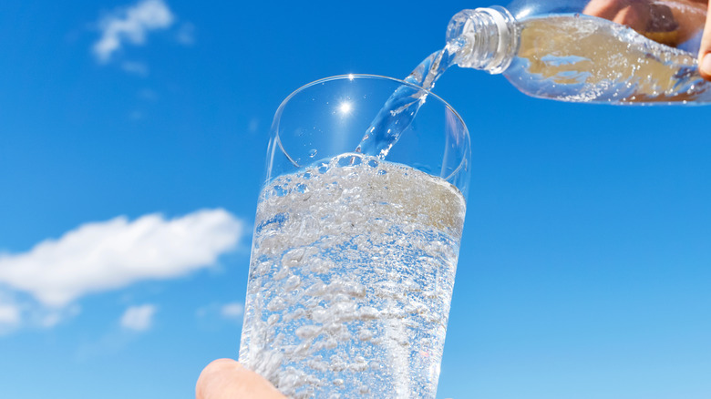 carbonated water being poured into glass in front of blue sky 