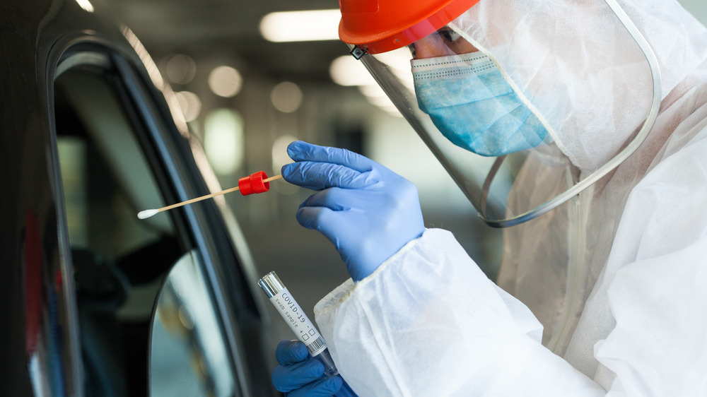 Medical worker in personal protective equipment swabbing a person in a car drive through Coronavirus COVID-19 mobile testing center