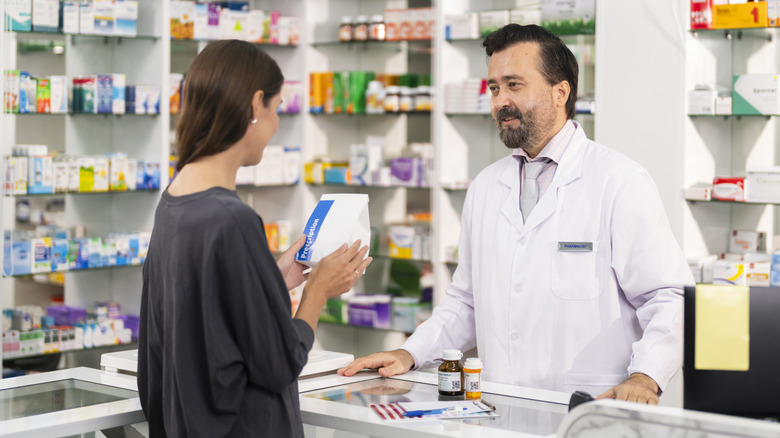 A woman holding her refilled prescription while talking with a pharmacist