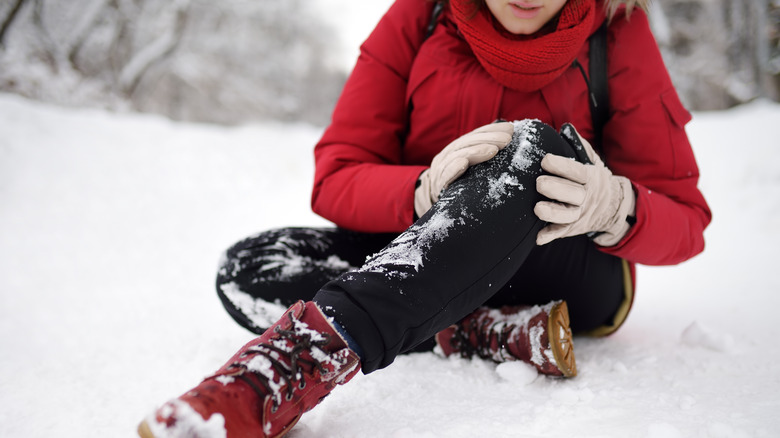 Fallen woman holding knee in snow