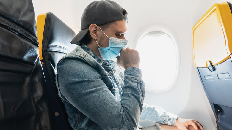 Masked man coughing on airplane