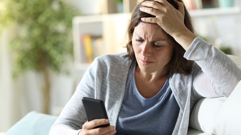 Woman reads phone at home with a look of worry on her face