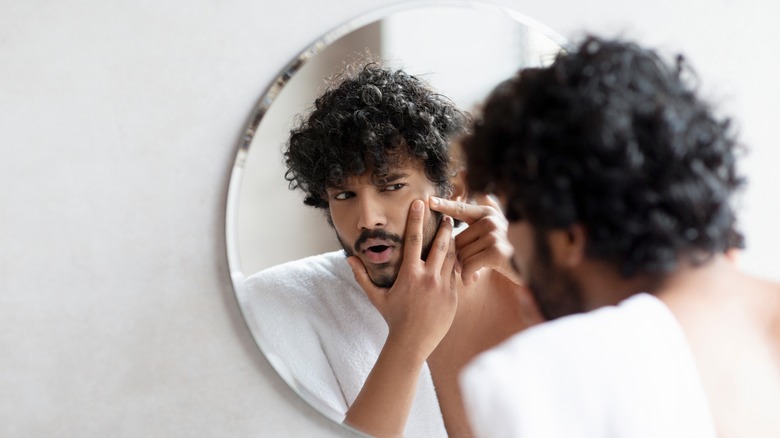 man inspecting pimple in mirror