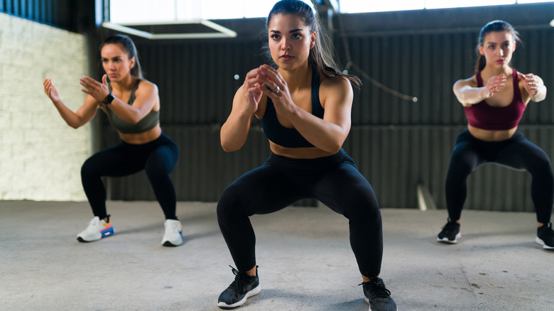 three women doing air squats in a fitness studio