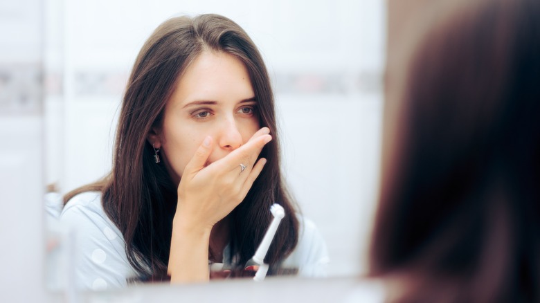 woman looking in mirror holding mouth