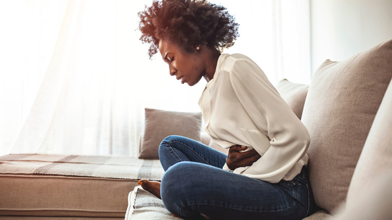 View of woman suffering from stomachache on sofa at home.