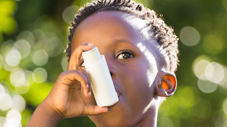 Child uses asthma inhaler outside in the park