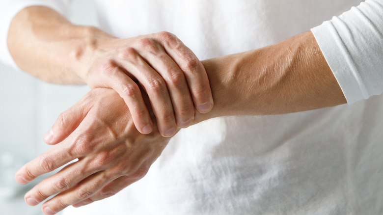 Person in white shirt holding hand and wrist