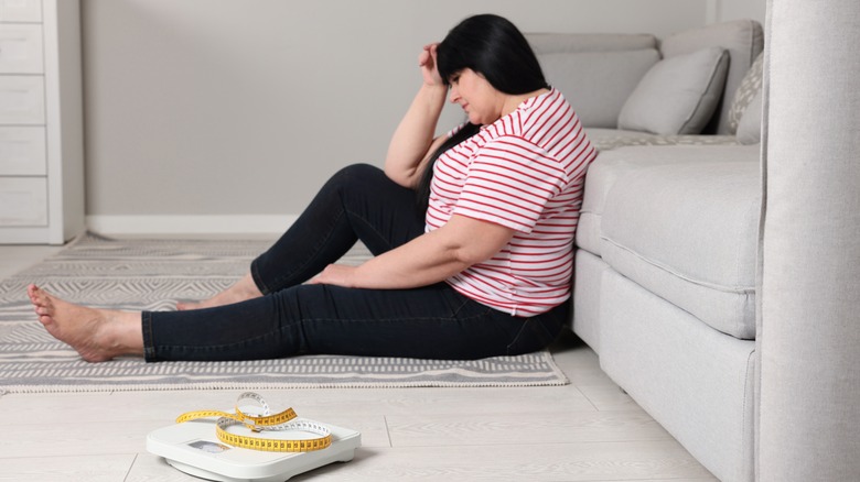 Overweight woman sitting next to scale