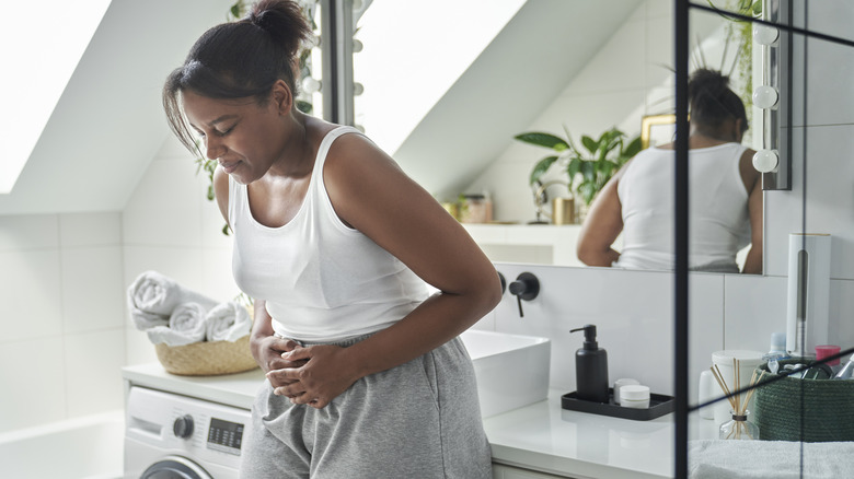 Woman standing in bathroom with stomach pain