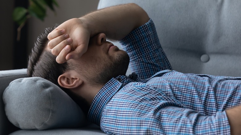 man lying on couch with arm over eyes