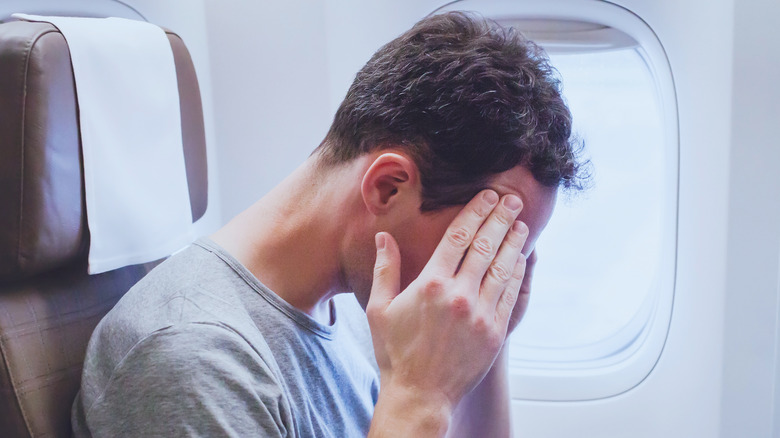 Man with a headache on an airplane, feeling bad during the flight