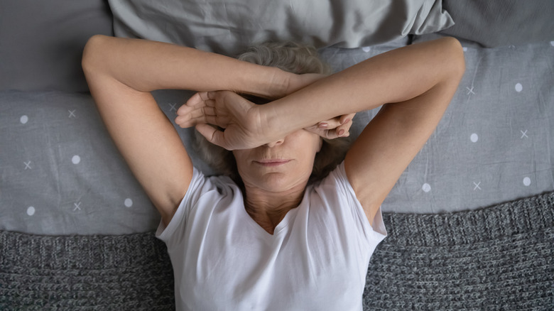 Older woman lying in bed covering her head with her arms