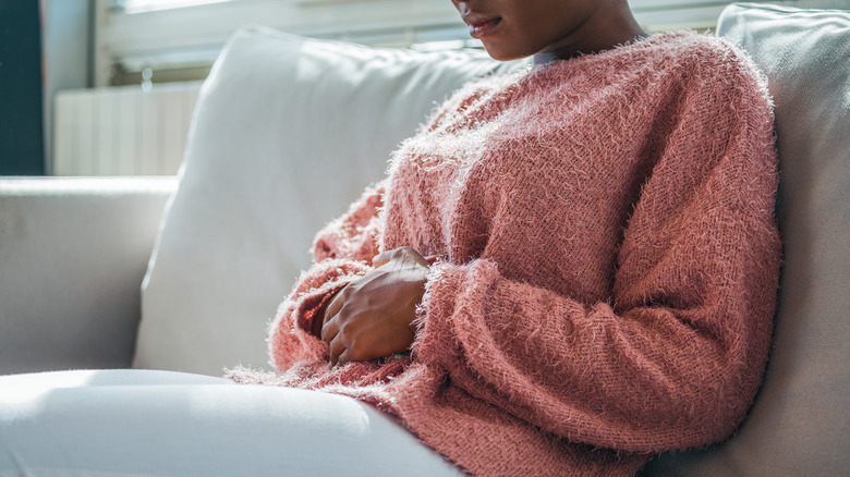 Woman sits on couch holding belly in pain