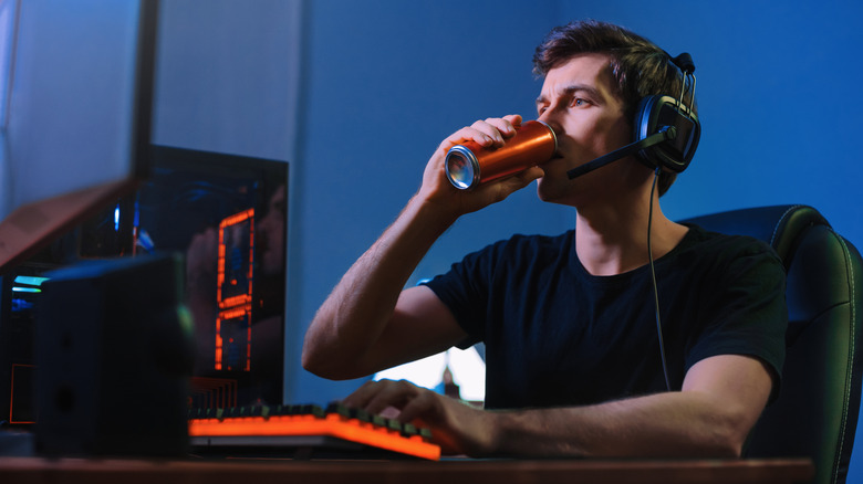 A man drinks an energy drink by his computer