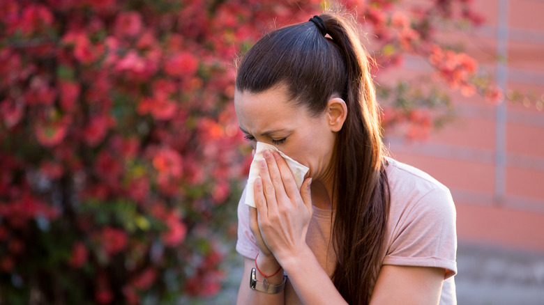 woman blows her nose in front of tree