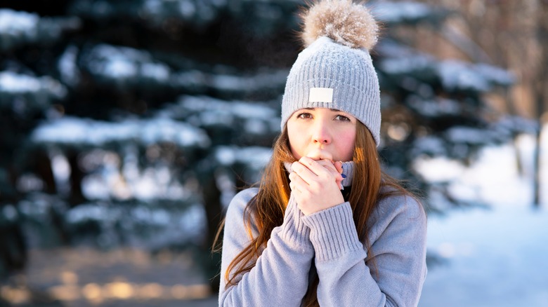 Woman outside in the cold blowing on her hands to keep warm