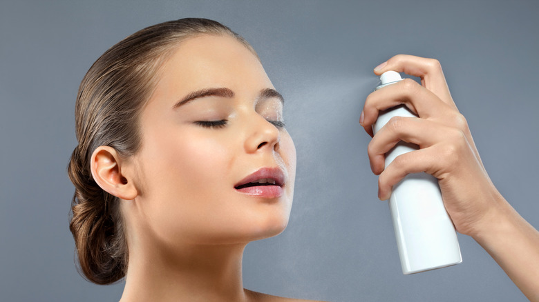 A woman sprays her face with cooling spray