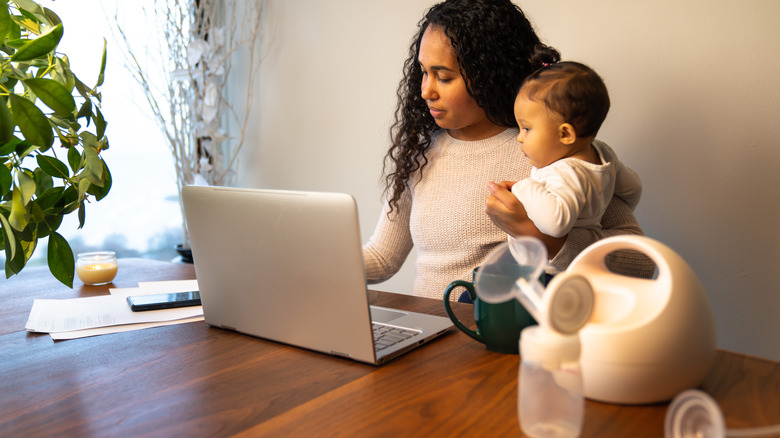 Mother holds baby sitting at table with breast pump nearby