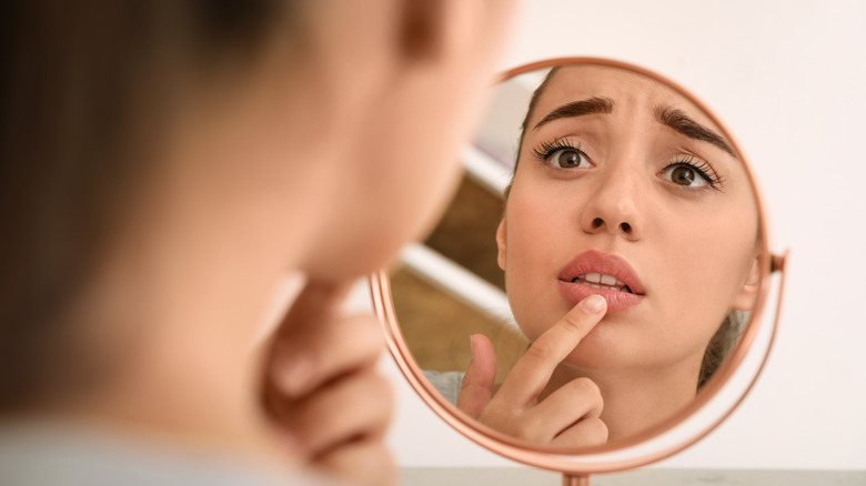 Woman looking at cold sore in mirror