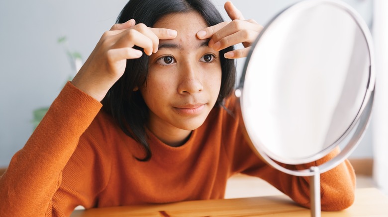 woman looking at her acne in mirror