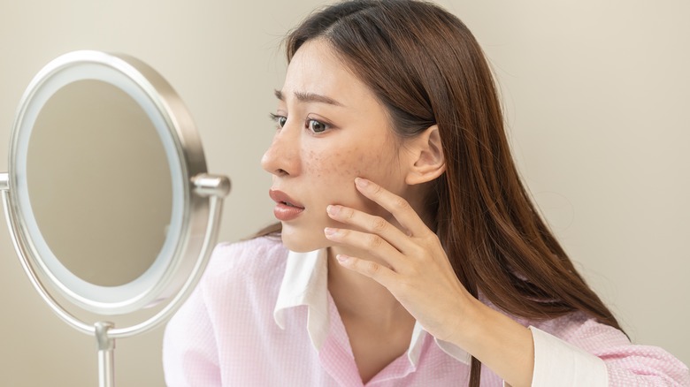 woman looking at acne in the mirror