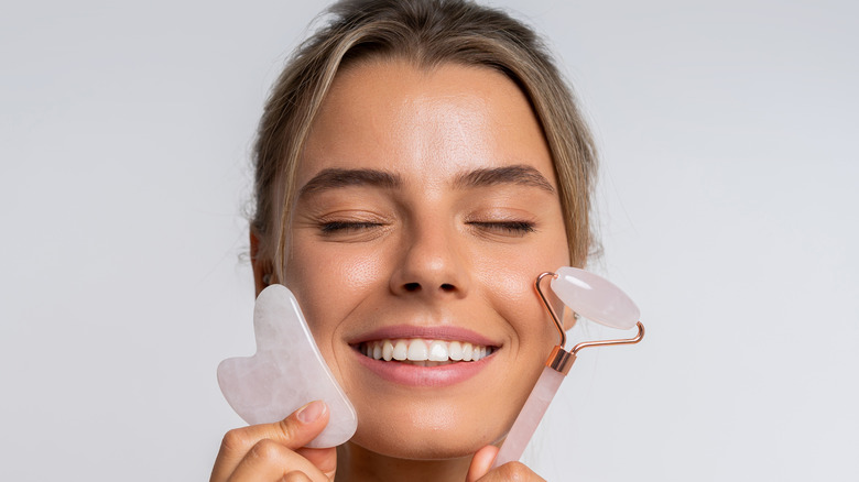 woman smiling as she holds two gua sha tools by her face