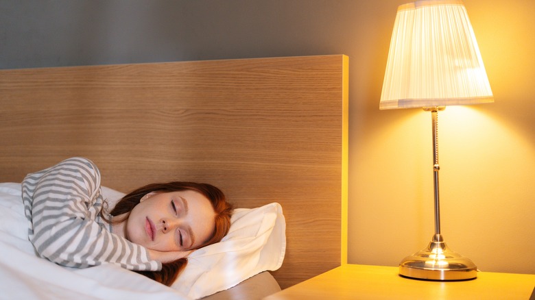 woman asleep in bed beside a lit table lamp