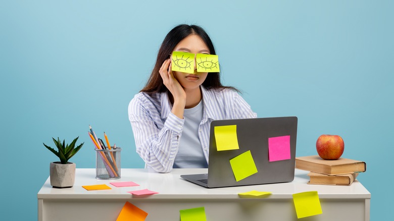 a woman with sticky notes all over her desk and over her eyes