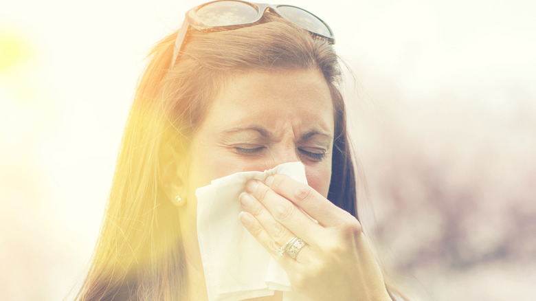 A woman sneezing outside under the sun