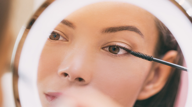 White woman applying mascara in front of a mirror