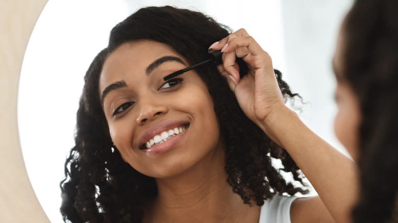 Smiling Black woman applying mascara in front of a mirror