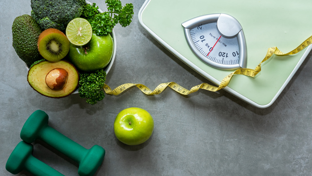 scale with healthy food and dumbbells