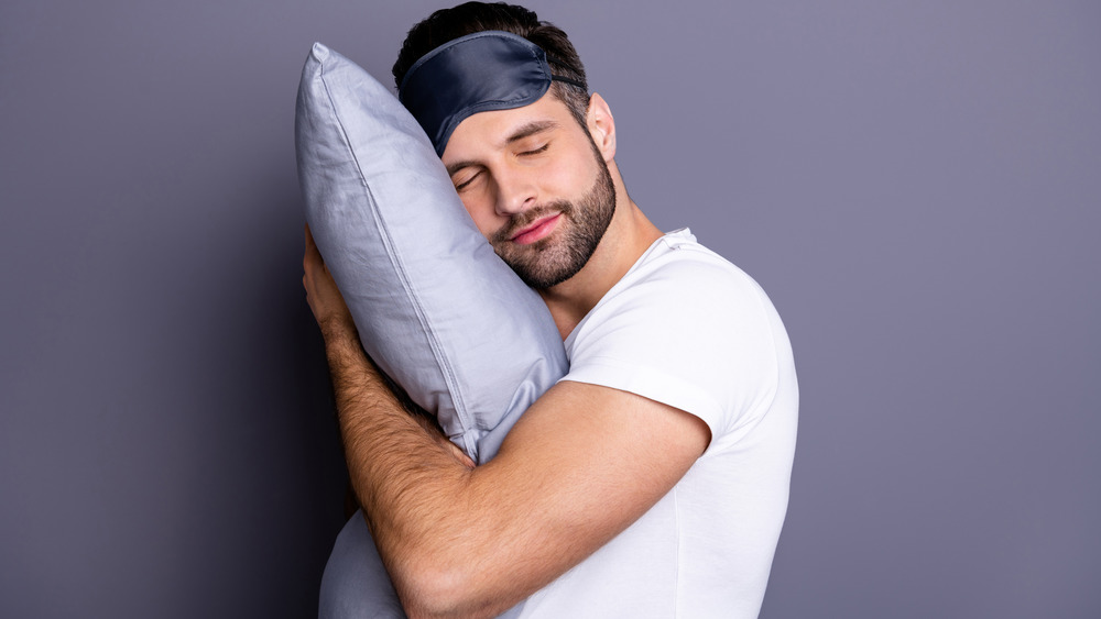 Man hugging pillow and wearing sleep mask on head