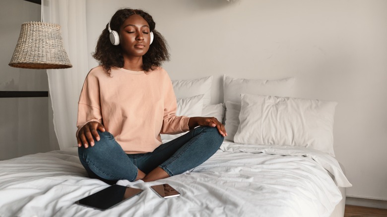 woman meditating on bed with headphones in