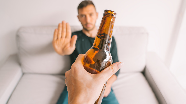 a man gesturing no to an offered bottle of beer 