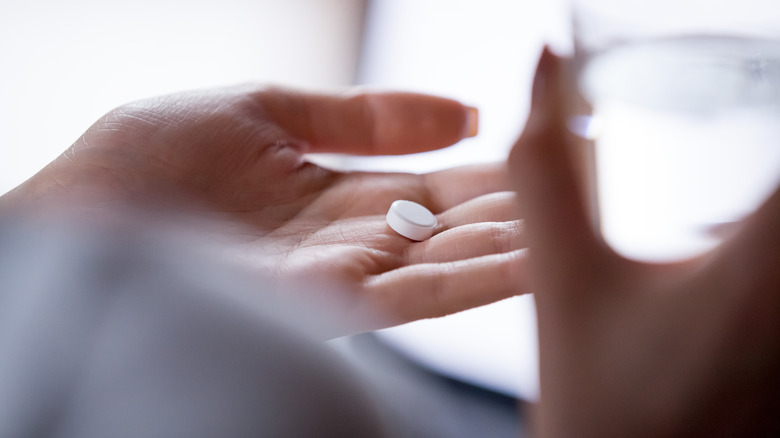 close up of woman holding pill in her hand with glass of water in the other hand